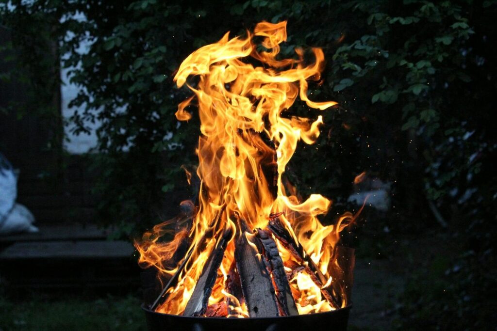 Bright campfire flames rise vividly against a dark outdoor backdrop, creating a dynamic and warm atmosphere.